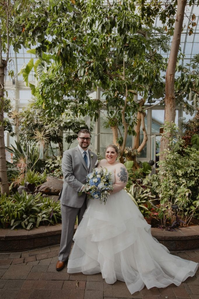 bride and groom pose together in front of foliage