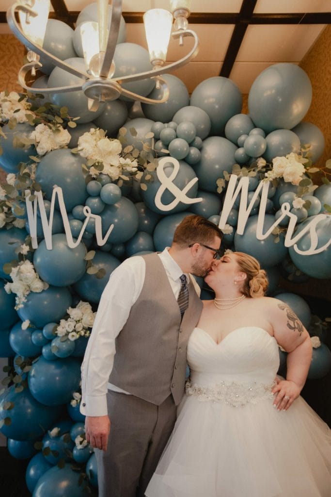 groom and bride kiss in front of balloons